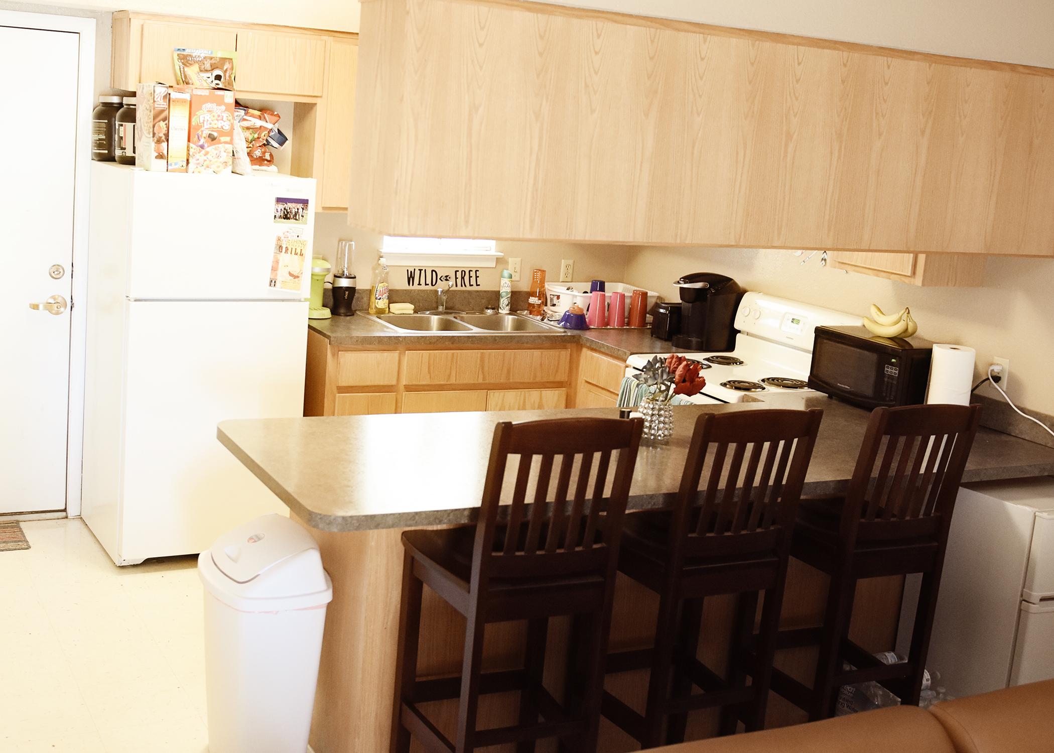 The kitchen area has four bar stools, a stove, and a refrigerator.